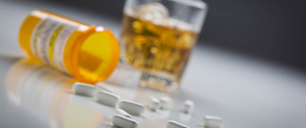 Several Prescription Drugs Spilled From Fallen Bottle Near Glass of Alcohol.